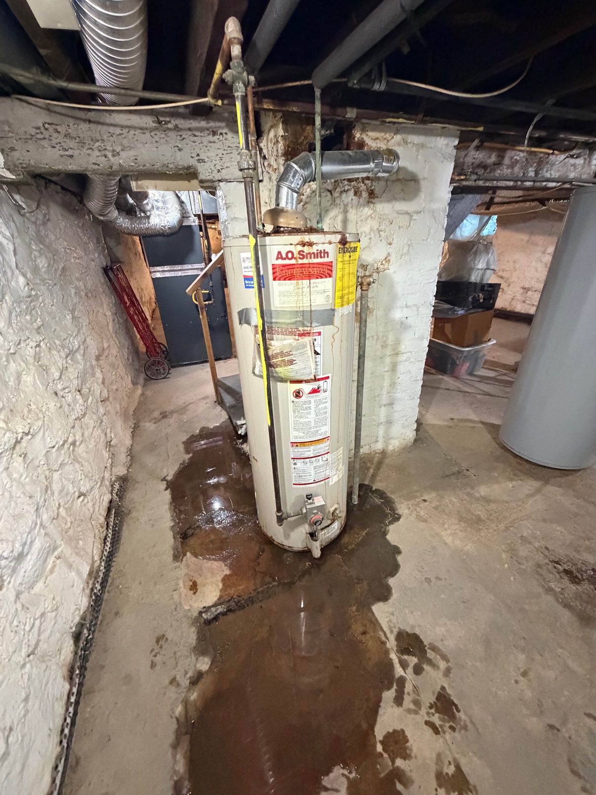 Before — a leaking A.O. Smith water heater with water pooled on the basement floor